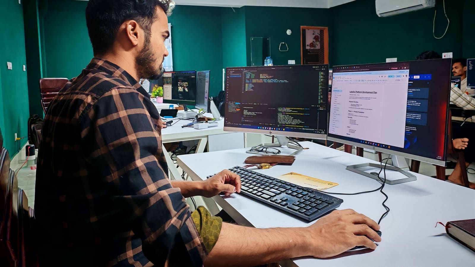A developer writes code on two monitors in an office with green walls