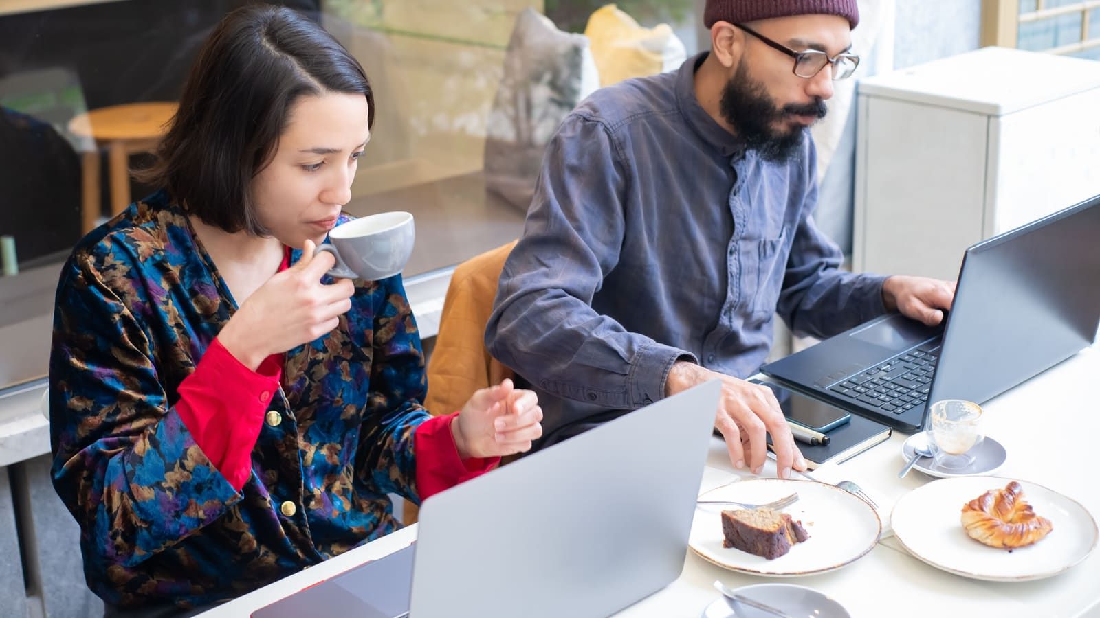 Two people work on laptops at a café table with coffee and pastries