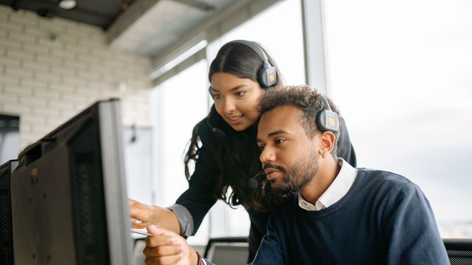 Two call center employees working together with headsets in a modern office setting