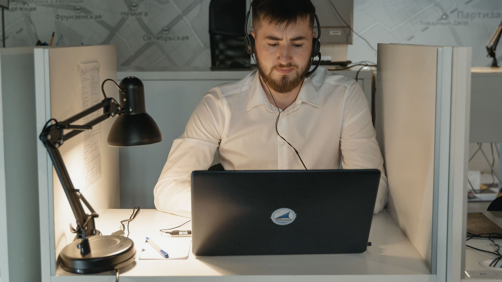 A support agent wearing a headset works on a laptop at his desk