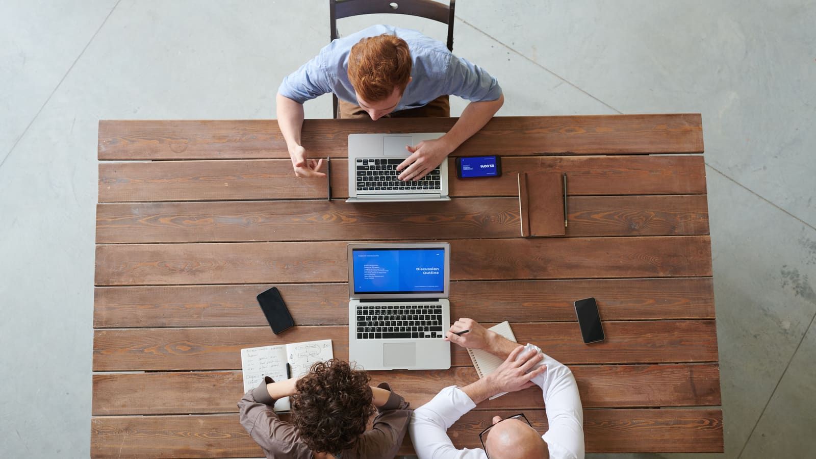 A team of three professionals collaborating at a wooden table with laptops and smartphones in a modern office