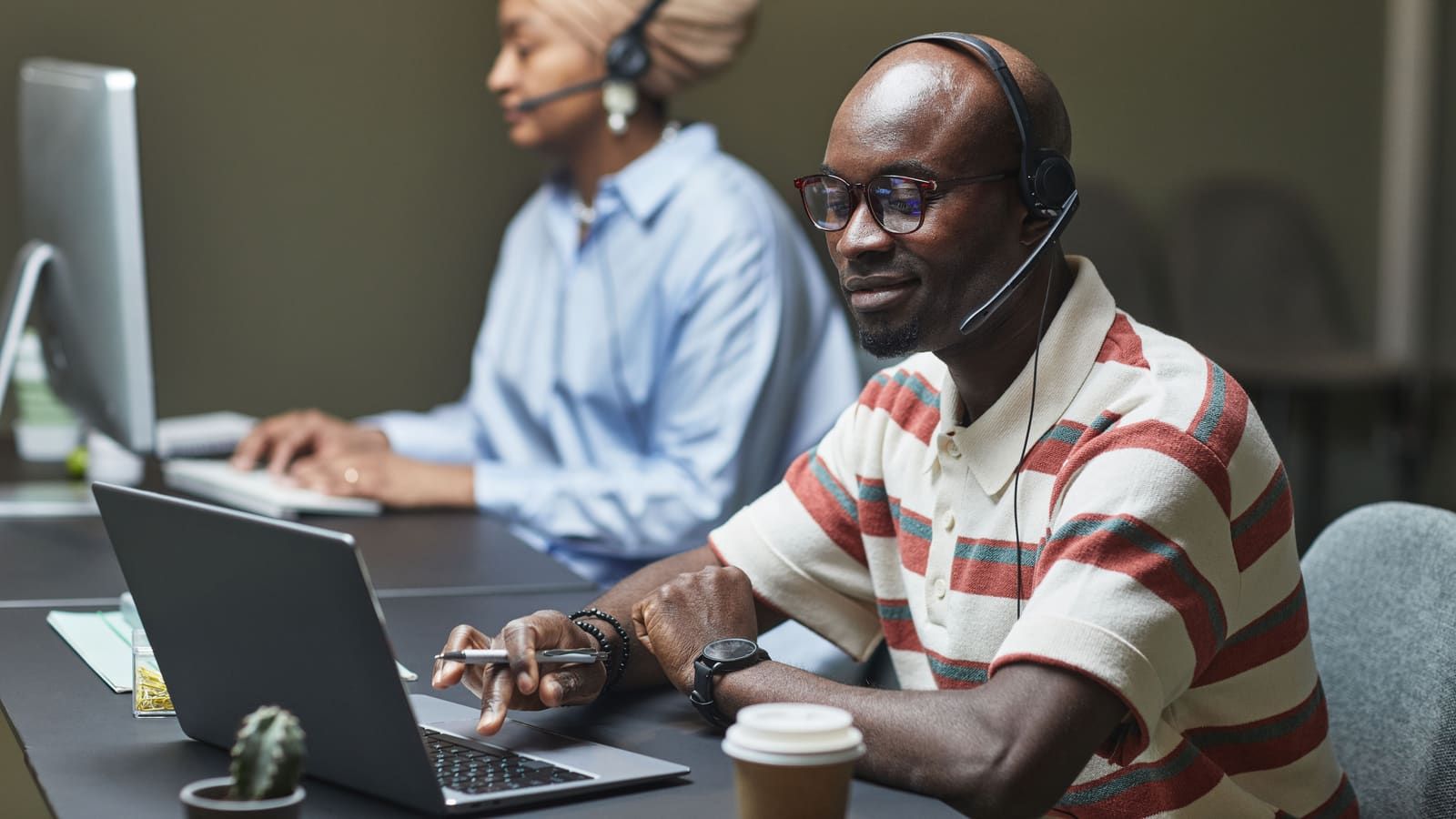 Two customer support employees working on computers with headsets in a modern office