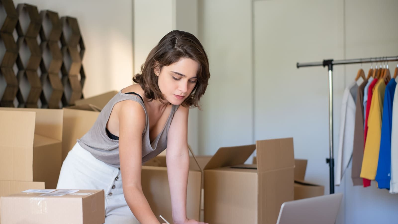 Young woman managing her online clothing business from home office with boxes and laptop