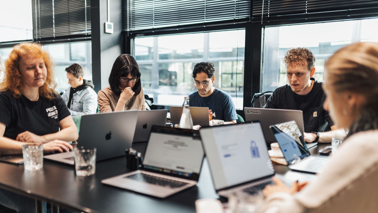 A small team works on laptops around a long table in an office