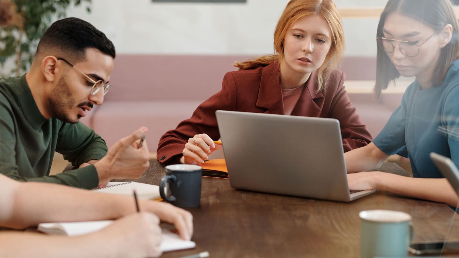 Three colleagues work together around a laptop at a wooden table