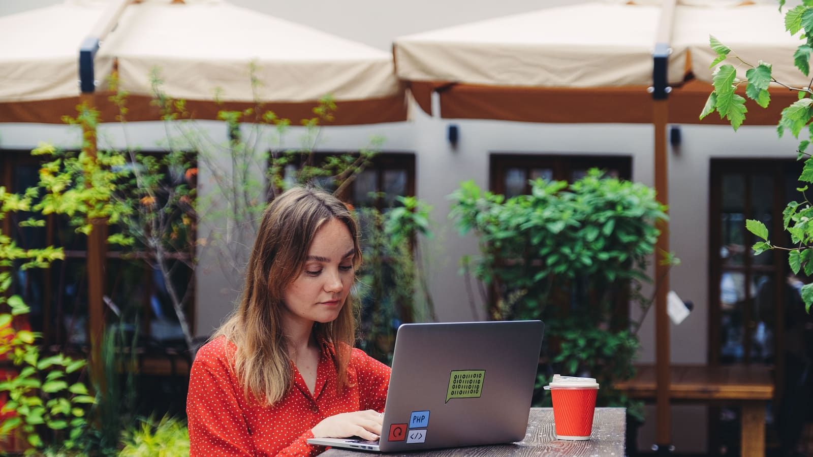 Young woman working on a laptop in an outdoor cafe setting, enjoying a cup of coffee