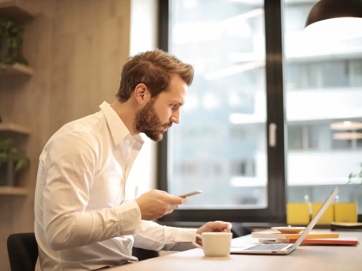 A founder calmly checking his phone at a sunny desk while the AI agent handles support